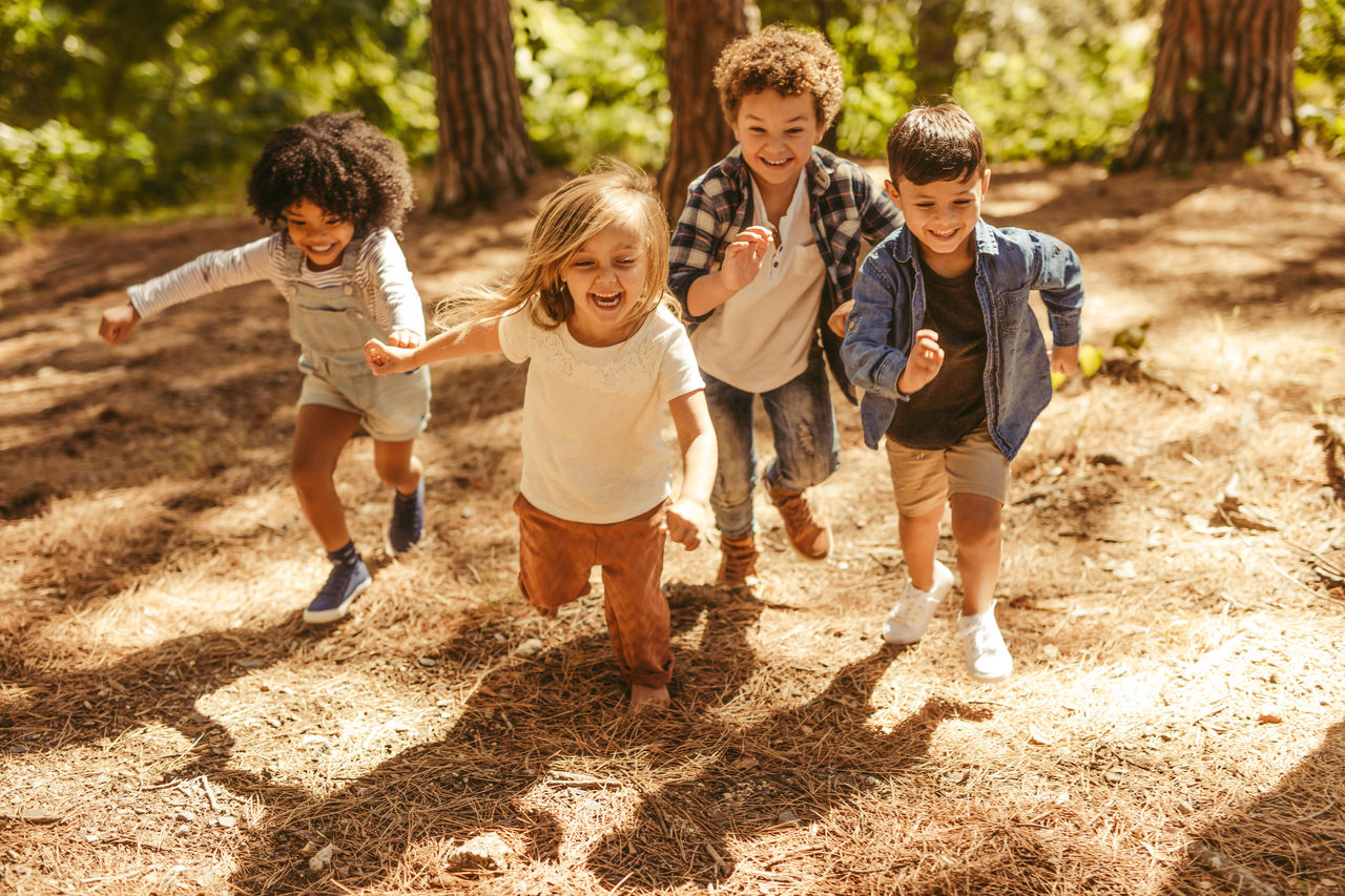 Group of kids running up in the forest. Multi-ethnic children playing together in forest.
