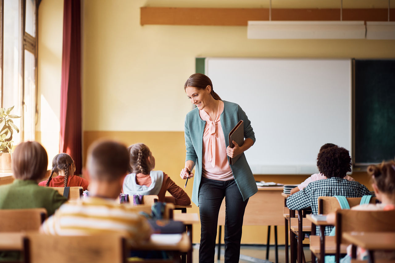 Happy teacher talks to schoolgirl during class in the classroom.